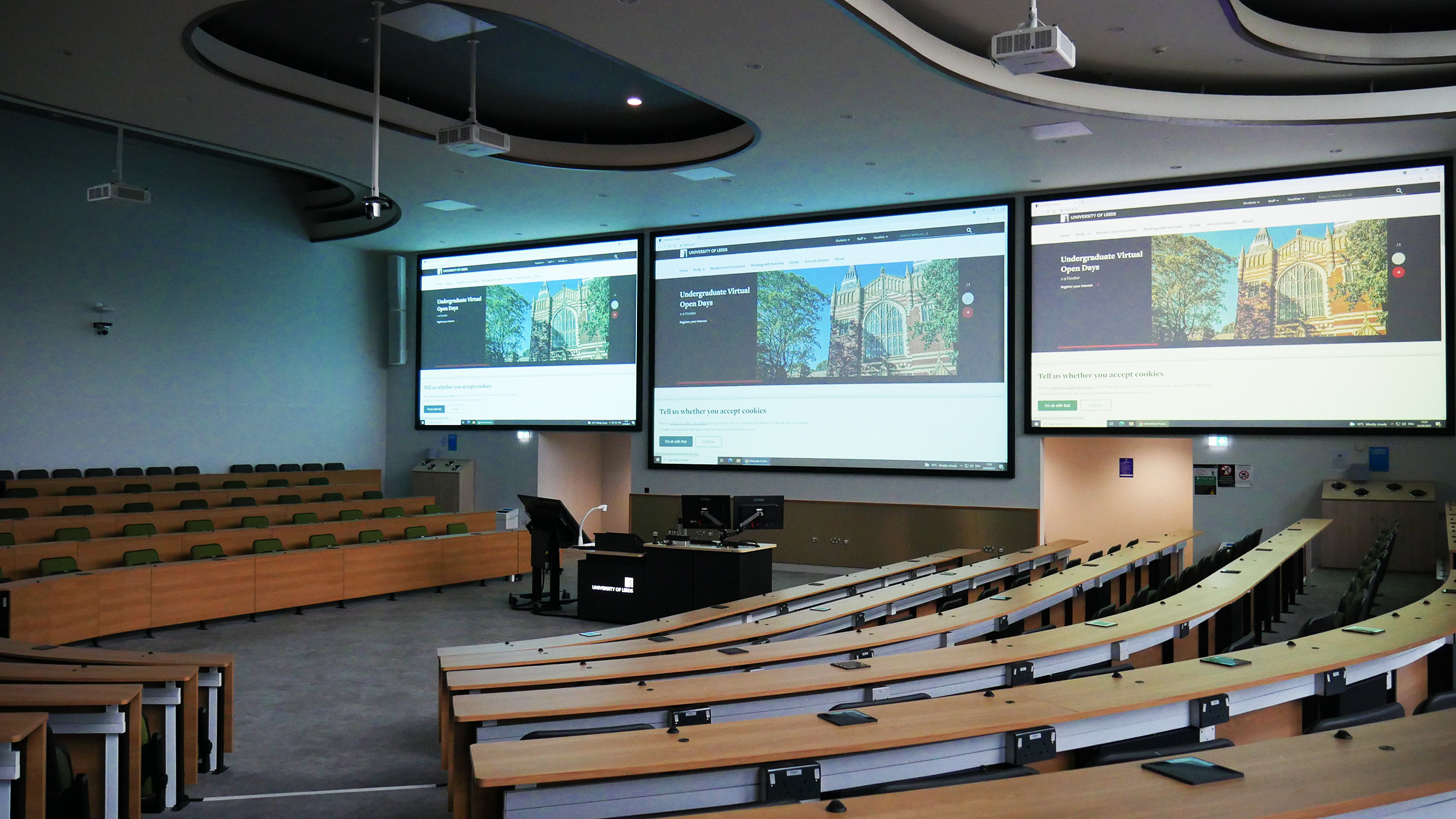 large university lecture theatre with three screens showing content
