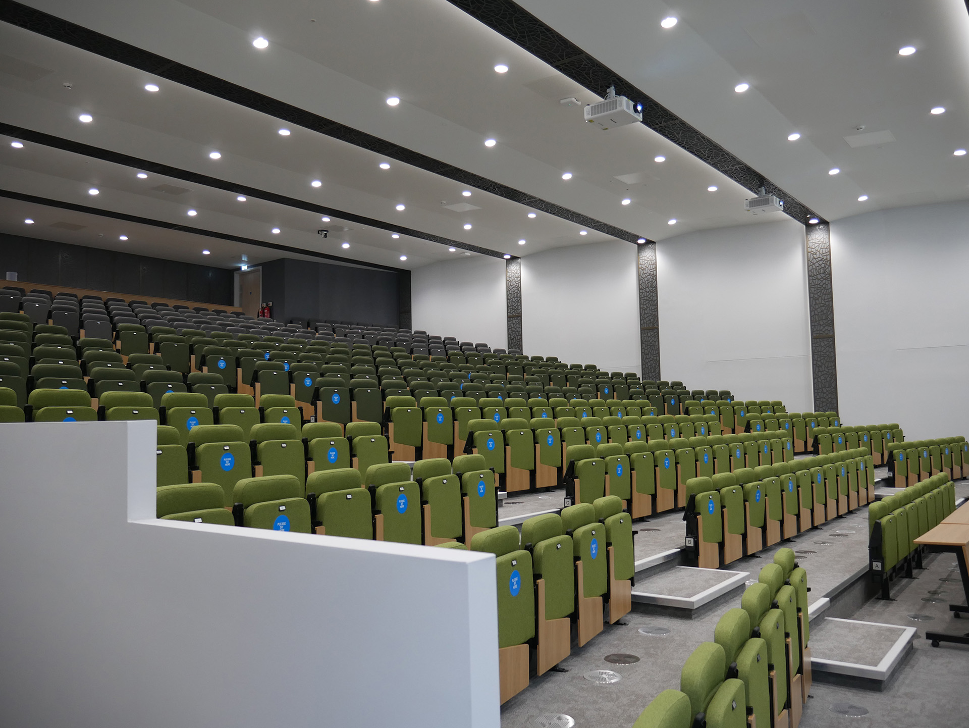 auditorium with green seating and projectors hanging from roof