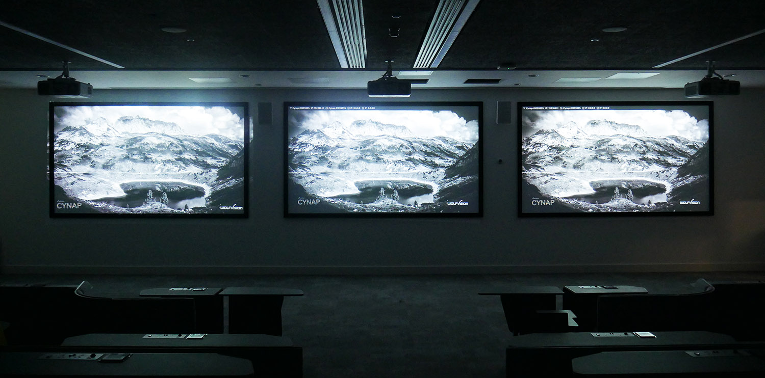 three projection screens at the front of a darkened lecture theatre